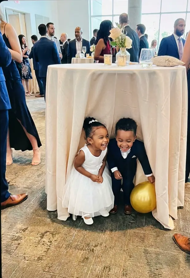 Two kids giggling under a reception table